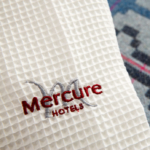 Close up of monogrammed Mercure Hotels dressing gown laid on a blue bedspread