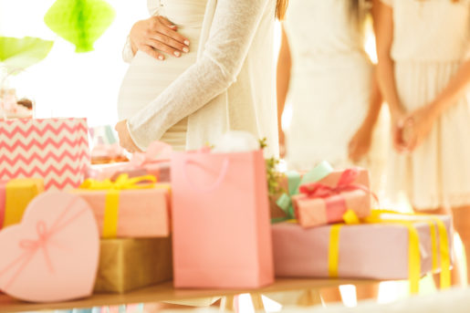 Mid section of pregnant woman holding her belly while standing by the table with a ppile of presents. Friends standing in the background.
