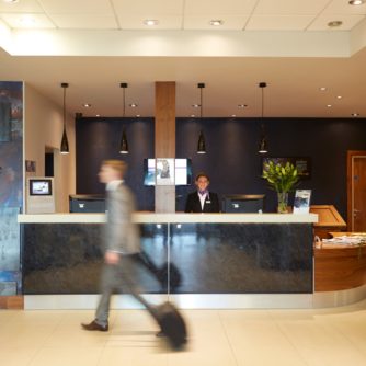 The reception desk at Mercure Sheffield Parkway Hotel, man in suit walks past in a blur, smiling receptionist