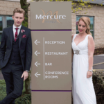 Bride and groom standing by the Mercure sign at Mercure Sheffield Parkway Hotel